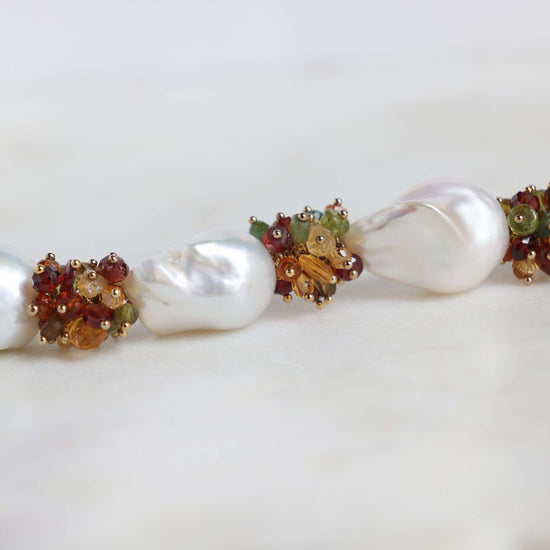 Close up of baroque pearl and gemstone beads inclueing opal, citrine, garnet,  and peridot